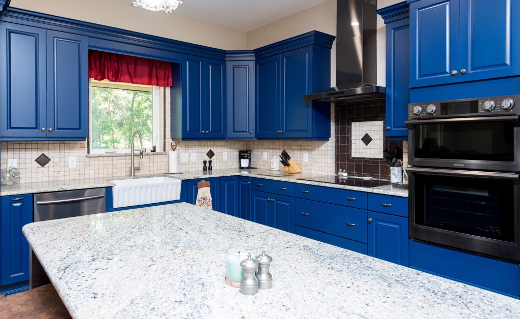 Kitchen with royal blue cabinets and red window treatments.
