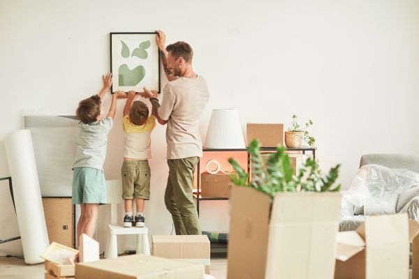 A father hangs an art print in a new home with the help of two young sons. 